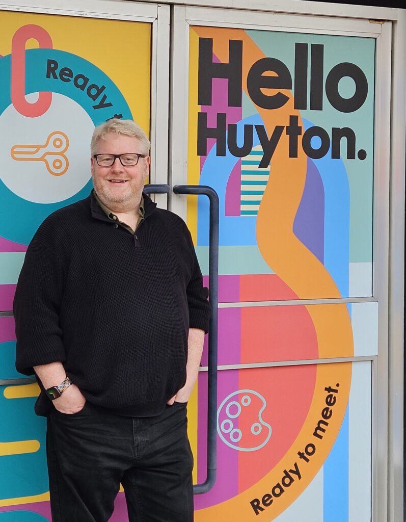 Tris Brown standing in front of the Hello Huyton sign