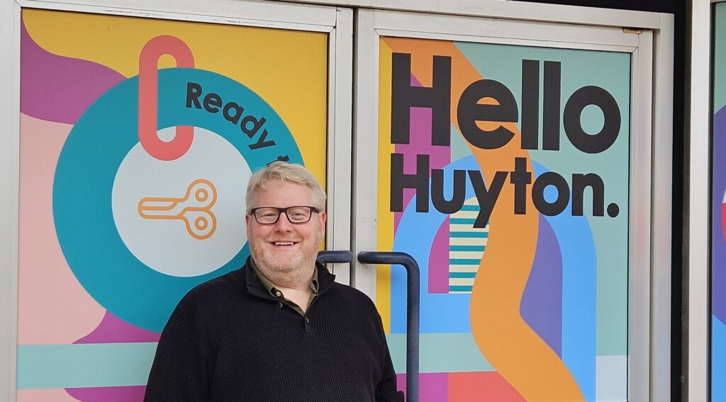 Tris Brown standing outside the Hello Huyton sign wide format